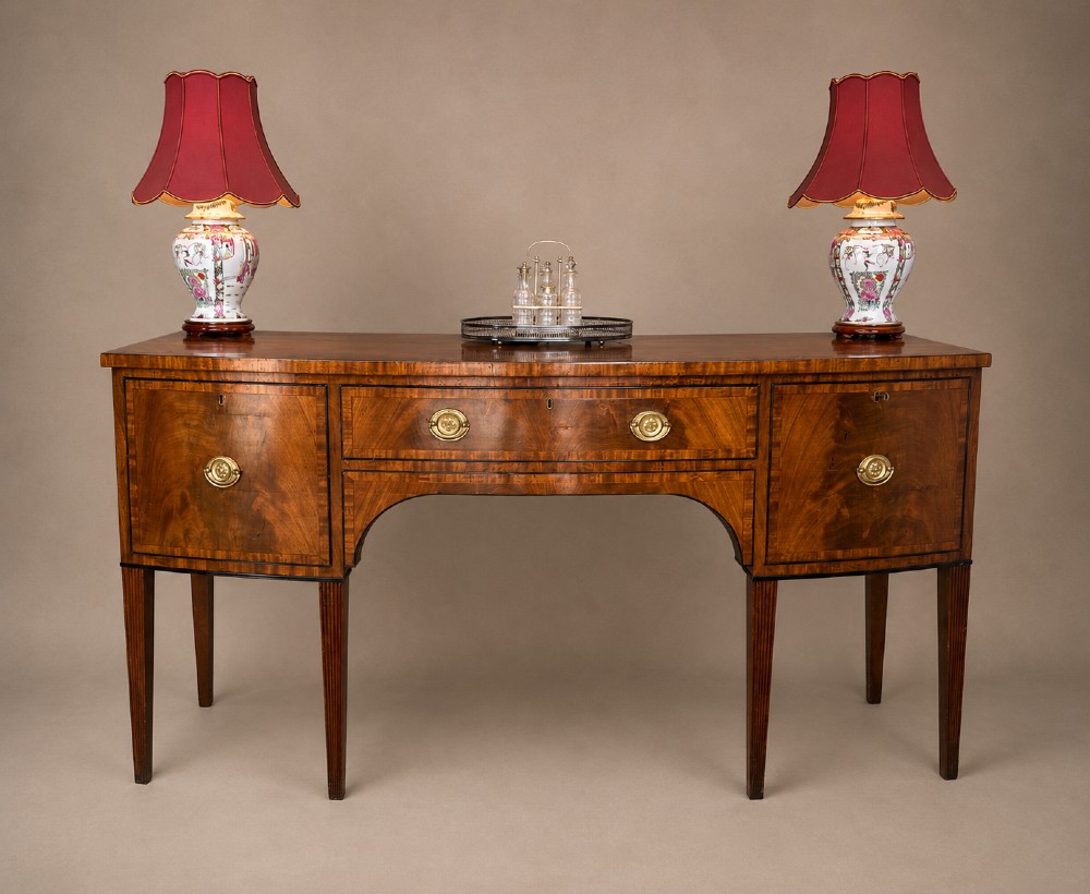 A Georgian mahogany sideboard featuring flame mahogany drawer fronts, brass ring handles, decorative line inlay, and fluted tapered legs.