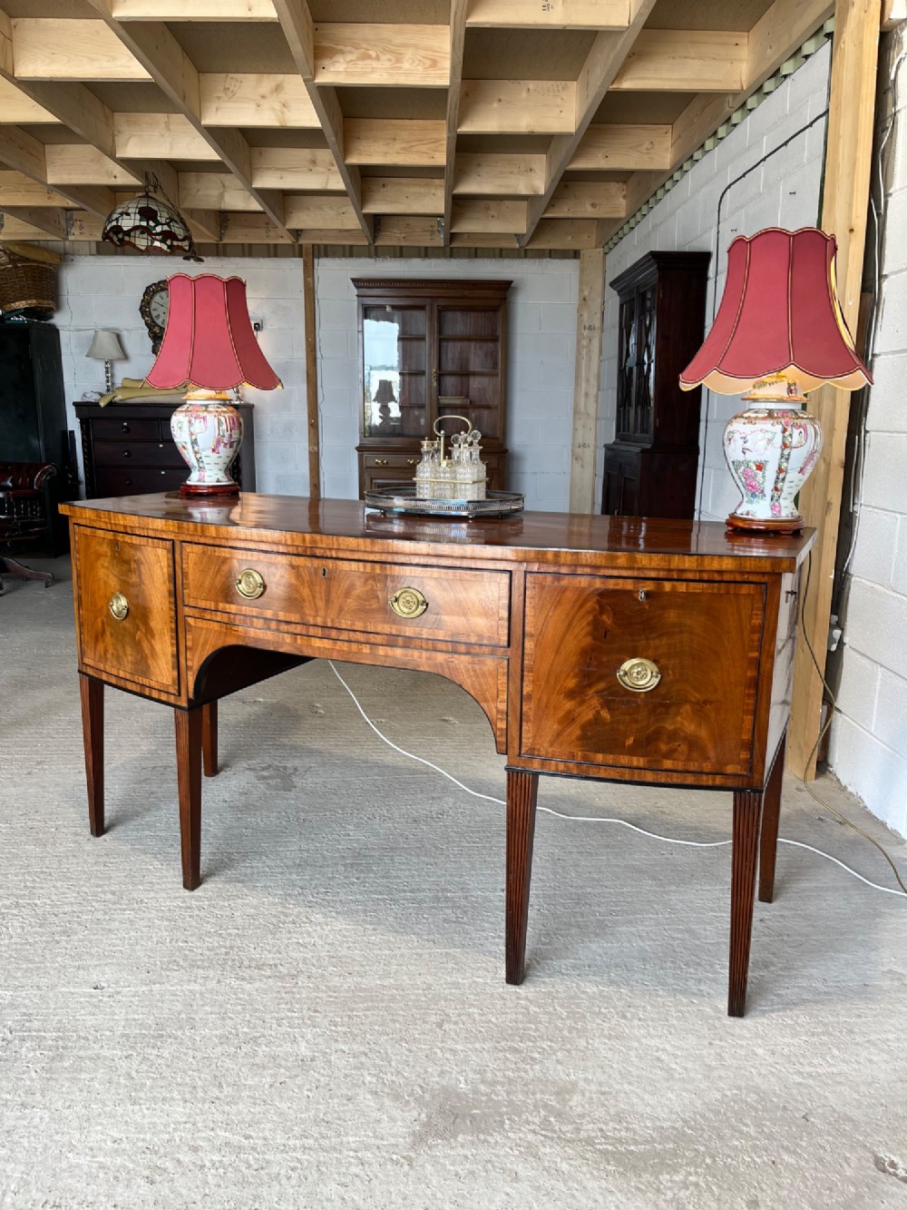 A Georgian mahogany sideboard featuring flame mahogany drawer fronts, brass ring handles, decorative line inlay, and fluted tapered legs. View IV