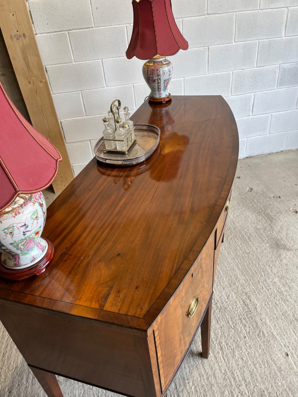 A Georgian mahogany sideboard featuring flame mahogany drawer fronts, brass ring handles, decorative line inlay, and fluted tapered legs. View V