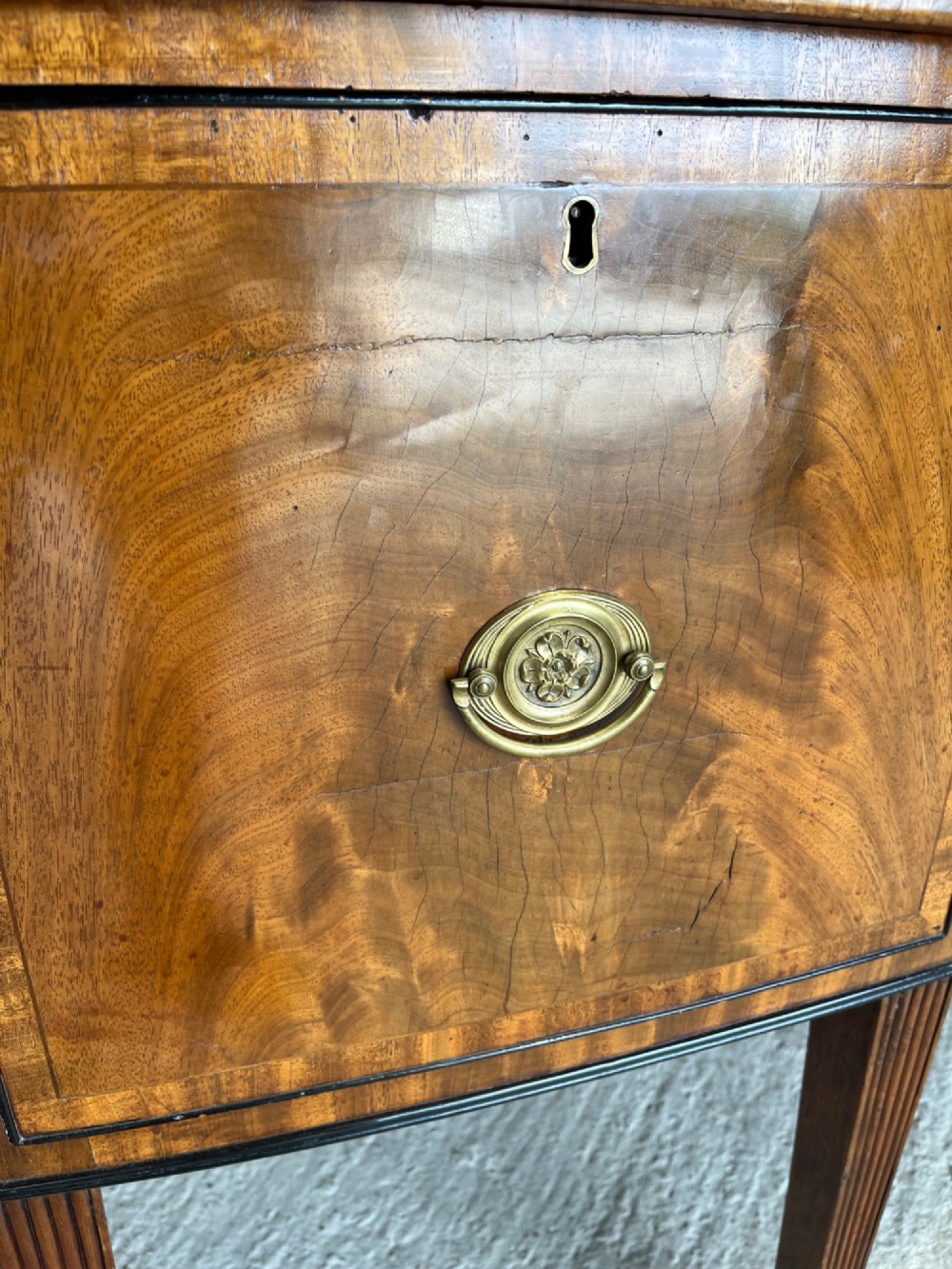 A Georgian mahogany sideboard featuring flame mahogany drawer fronts, brass ring handles, decorative line inlay, and fluted tapered legs. View VI