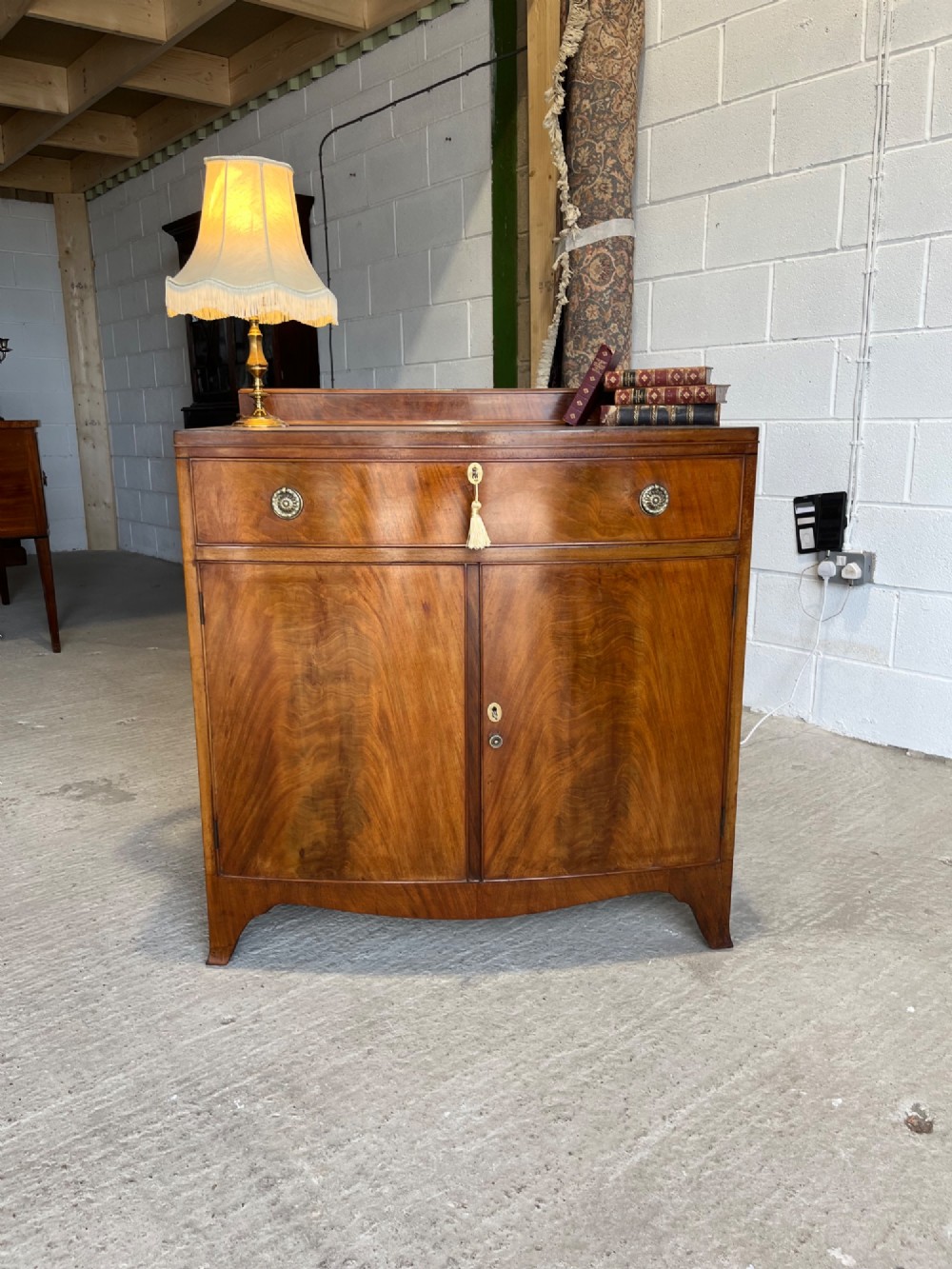 A late 19th-century mahogany cupboard featuring a single top drawer over a two-door cabinet with flame mahogany veneer panels and turned brass ring pull handles. View II