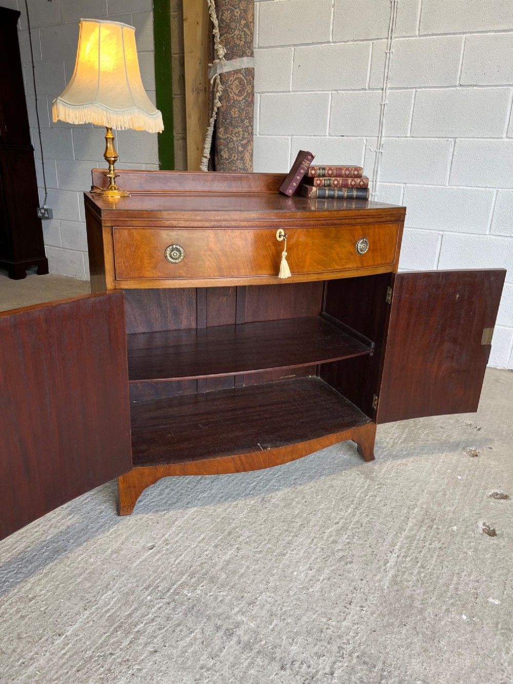 A late 19th-century mahogany cupboard featuring a single top drawer over a two-door cabinet with flame mahogany veneer panels and turned brass ring pull handles. View V