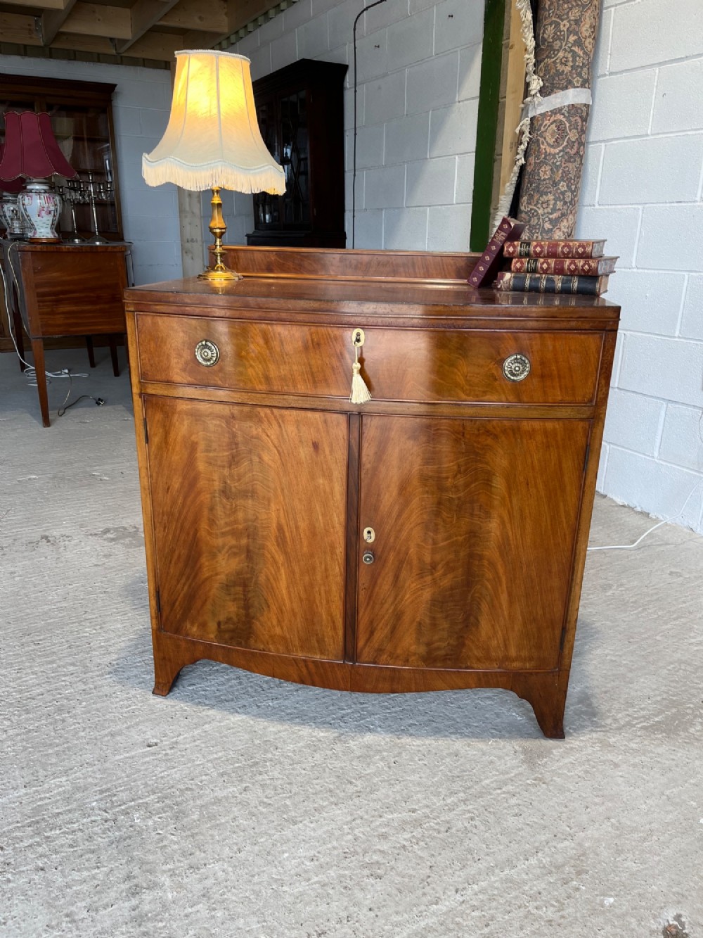 A late 19th-century mahogany cupboard featuring a single top drawer over a two-door cabinet with flame mahogany veneer panels and turned brass ring pull handles. View VII