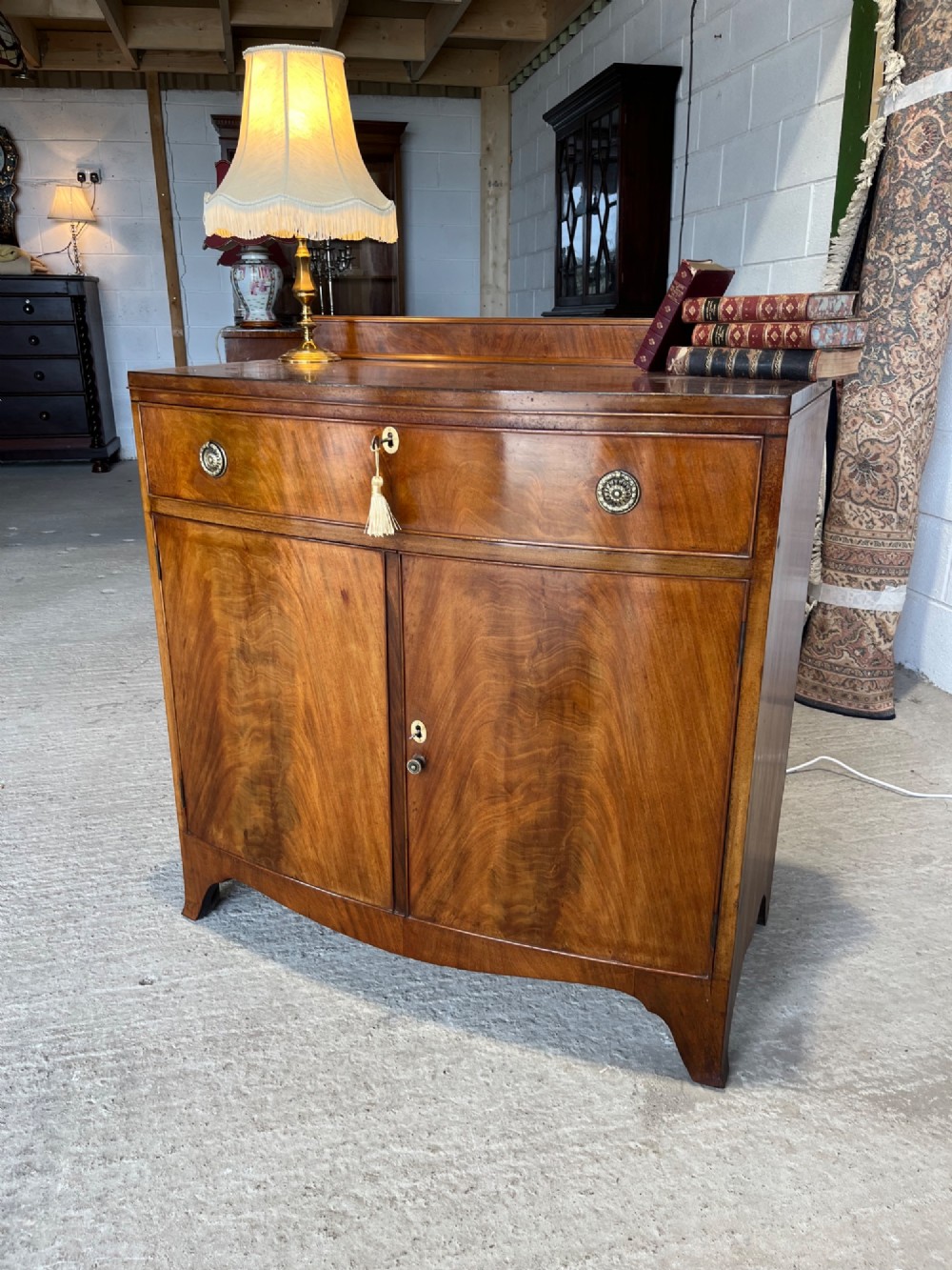 A late 19th-century mahogany cupboard featuring a single top drawer over a two-door cabinet with flame mahogany veneer panels and turned brass ring pull handles. View XI