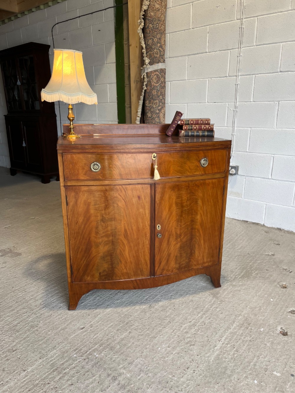 A late 19th-century mahogany cupboard featuring a single top drawer over a two-door cabinet with flame mahogany veneer panels and turned brass ring pull handles. View XII