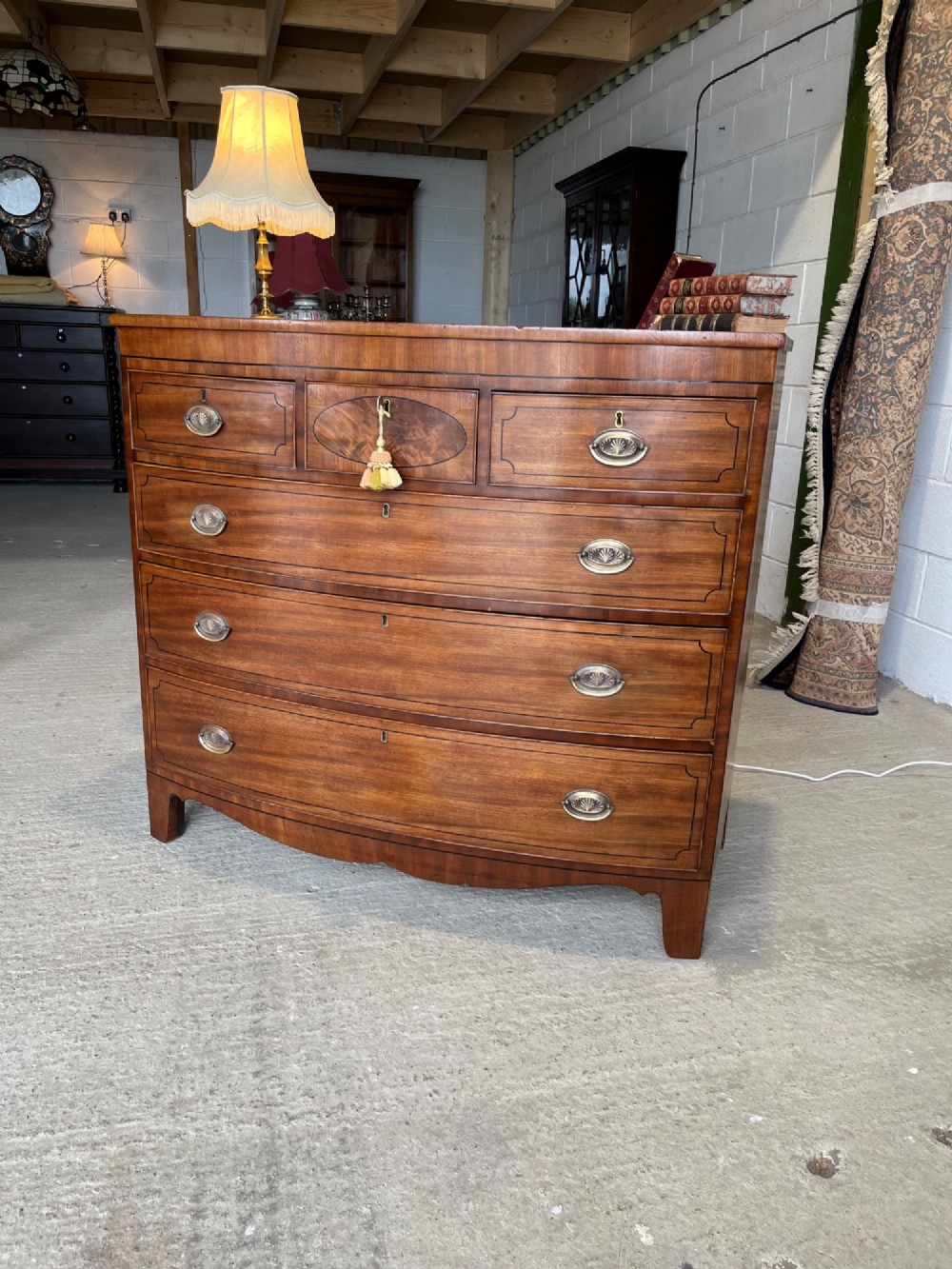 A 19th-century mahogany bowfront chest of drawers featuring a curved front with multiple drawers, brass oval drop handles, keyhole escutcheons, and bracket feet. View II