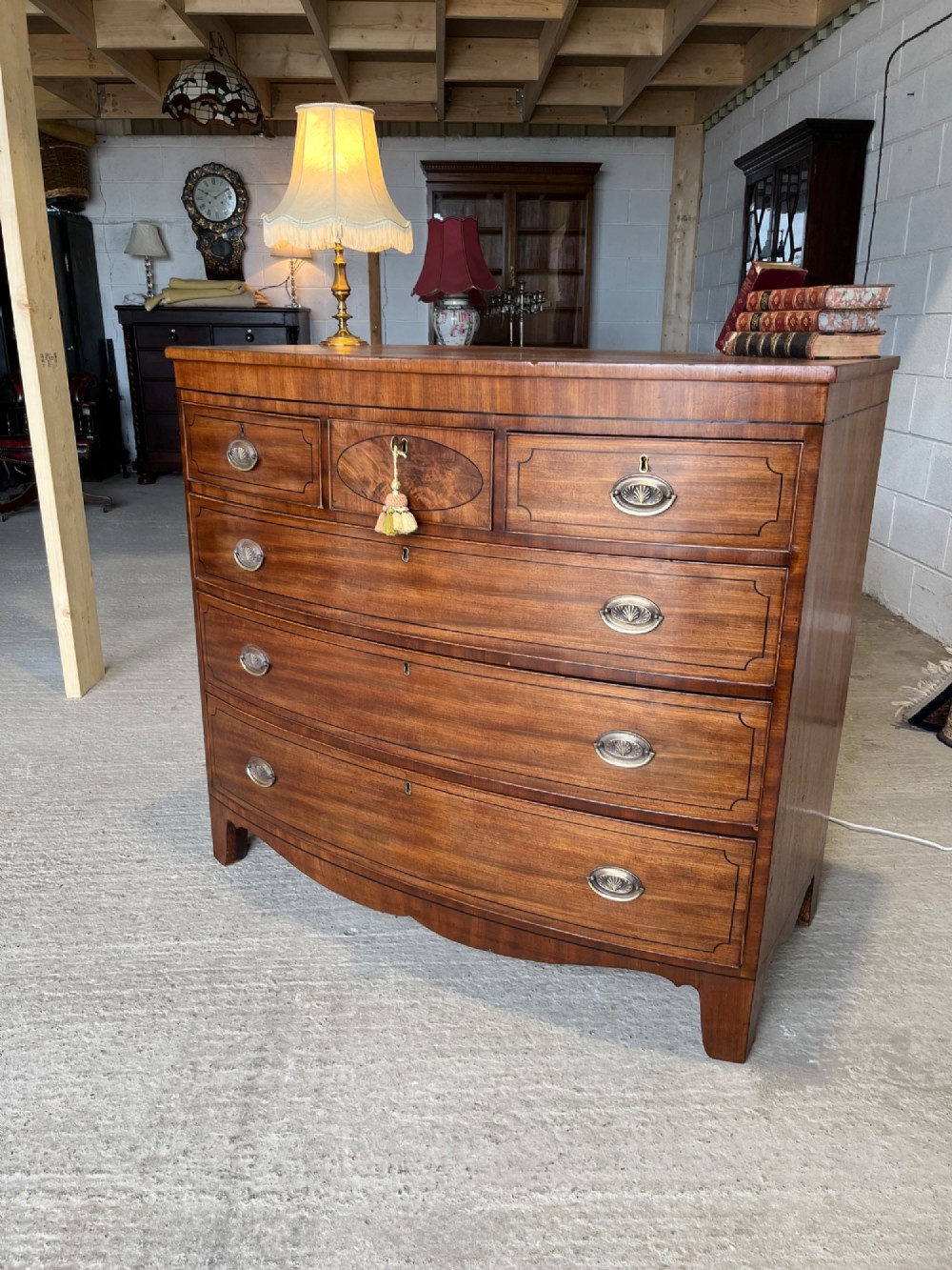 A 19th-century mahogany bowfront chest of drawers featuring a curved front with multiple drawers, brass oval drop handles, keyhole escutcheons, and bracket feet. View V
