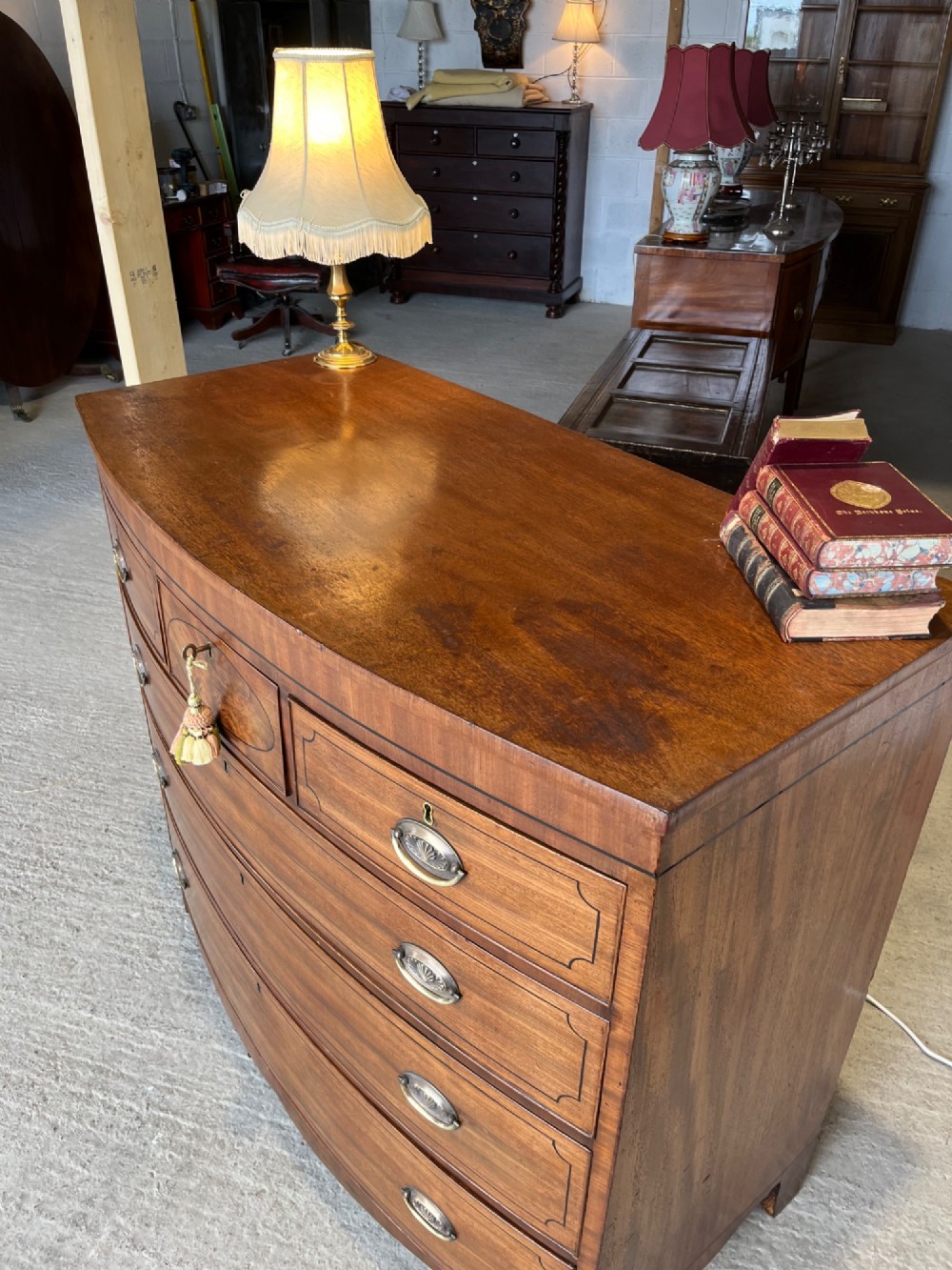 A 19th-century mahogany bowfront chest of drawers featuring a curved front with multiple drawers, brass oval drop handles, keyhole escutcheons, and bracket feet. View VI