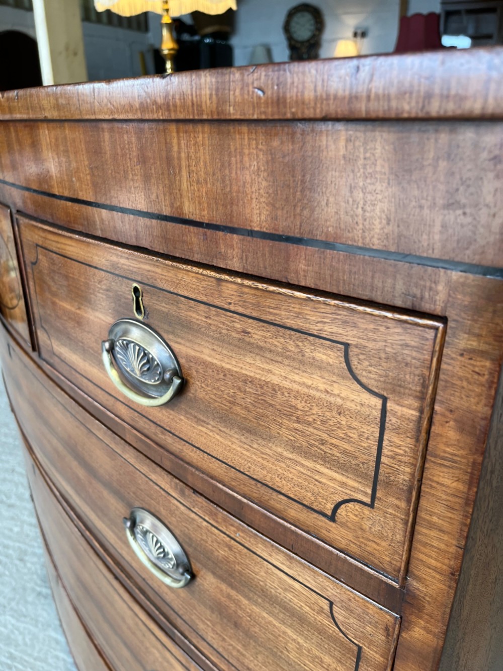 A 19th-century mahogany bowfront chest of drawers featuring a curved front with multiple drawers, brass oval drop handles, keyhole escutcheons, and bracket feet. View VII