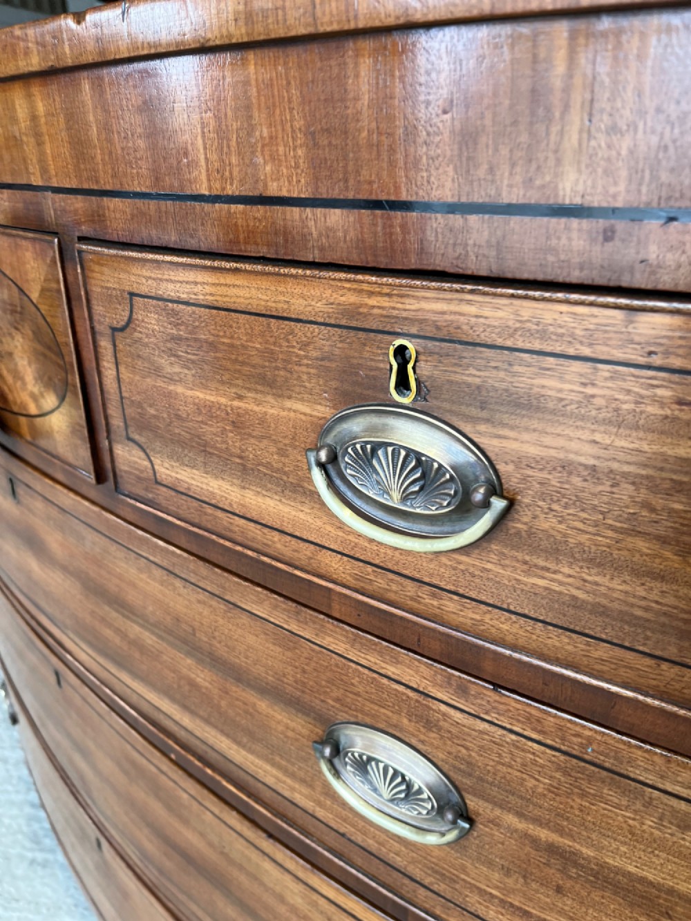 A 19th-century mahogany bowfront chest of drawers featuring a curved front with multiple drawers, brass oval drop handles, keyhole escutcheons, and bracket feet. View VIII