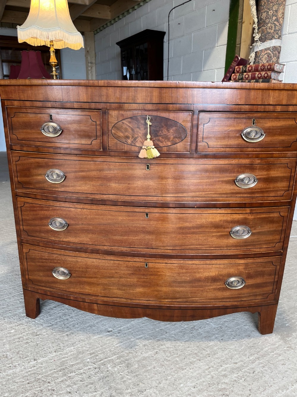 A 19th-century mahogany bowfront chest of drawers featuring a curved front with multiple drawers, brass oval drop handles, keyhole escutcheons, and bracket feet. View X