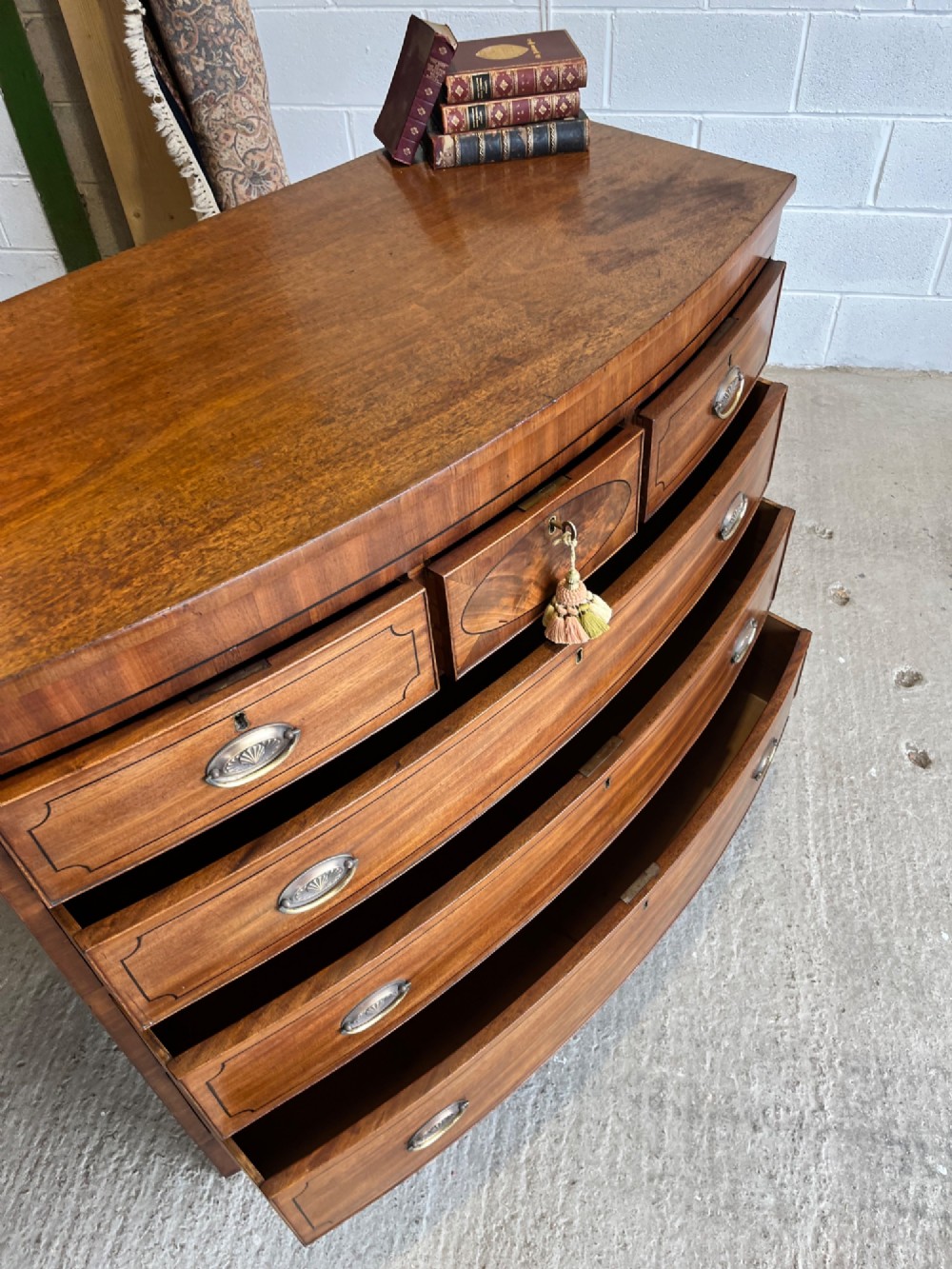 A 19th-century mahogany bowfront chest of drawers featuring a curved front with multiple drawers, brass oval drop handles, keyhole escutcheons, and bracket feet. View XI