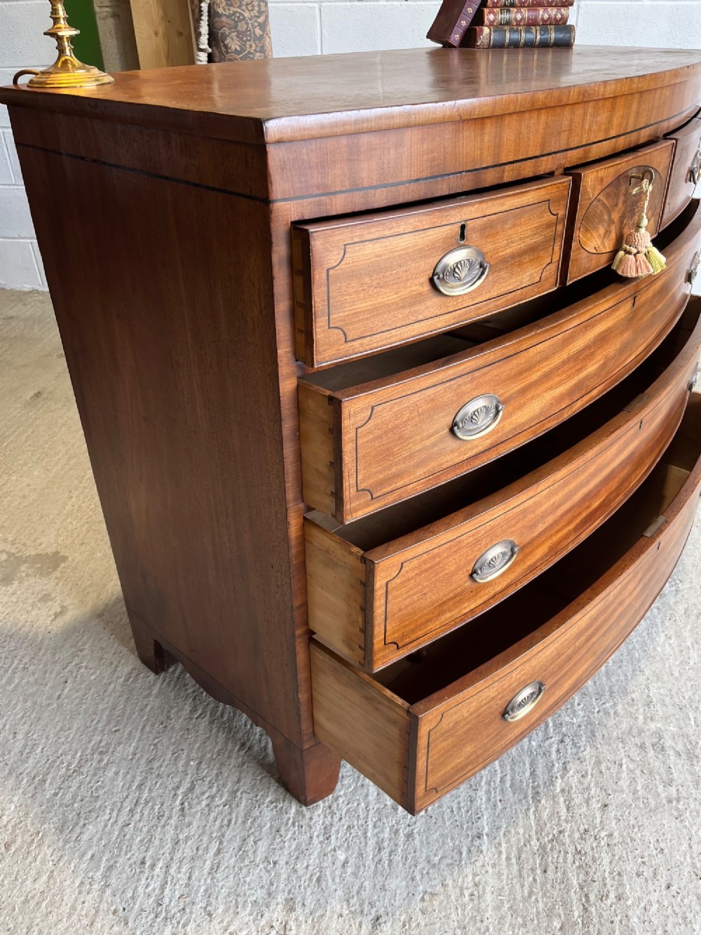 A 19th-century mahogany bowfront chest of drawers featuring a curved front with multiple drawers, brass oval drop handles, keyhole escutcheons, and bracket feet. View XII