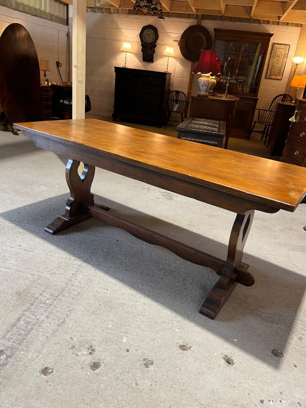 A long solid oak refectory table with a trestle base, surrounded by eight ladderback dining chairs with woven rush seats. View V