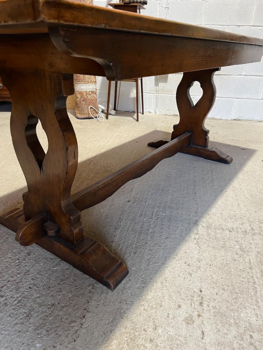 A long solid oak refectory table with a trestle base, surrounded by eight ladderback dining chairs with woven rush seats. View X