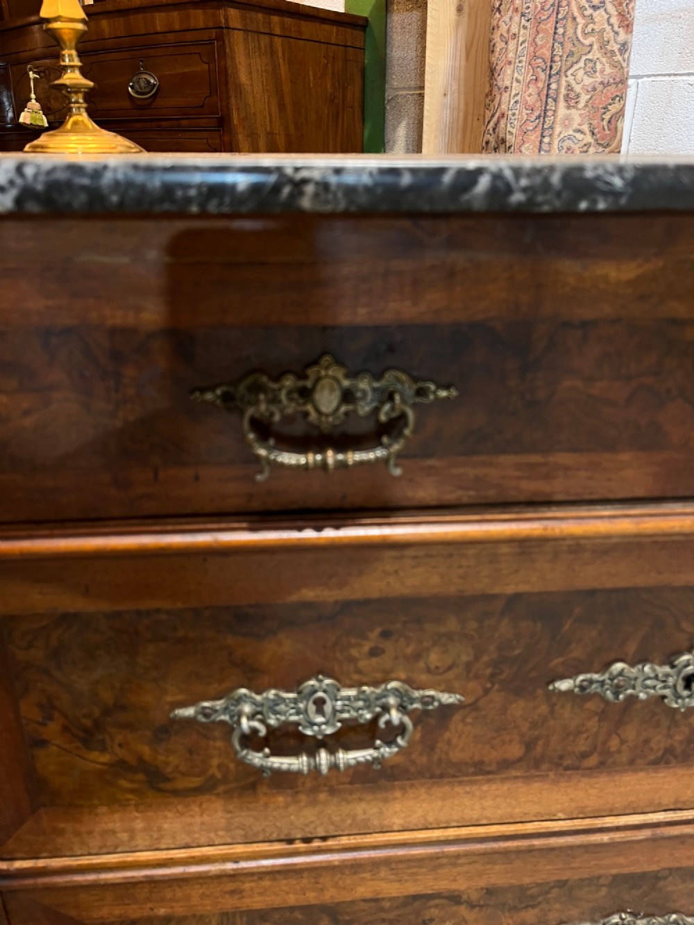 An antique 19th-century French walnut chest of drawers featuring a dark grey marble top and ornate brass handles. View IX