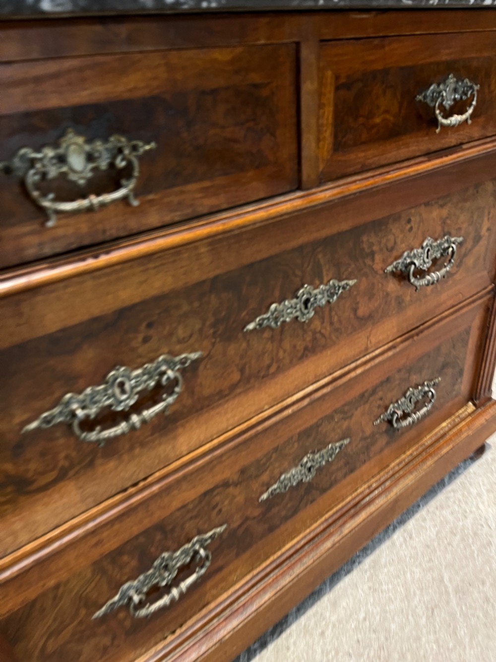An antique 19th-century French walnut chest of drawers featuring a dark grey marble top and ornate brass handles. View X