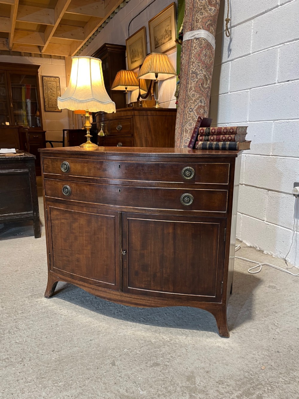 An early 20th-century mahogany bowfront cupboard with two top drawers featuring brass ring handles above a double-door lower compartment. View II