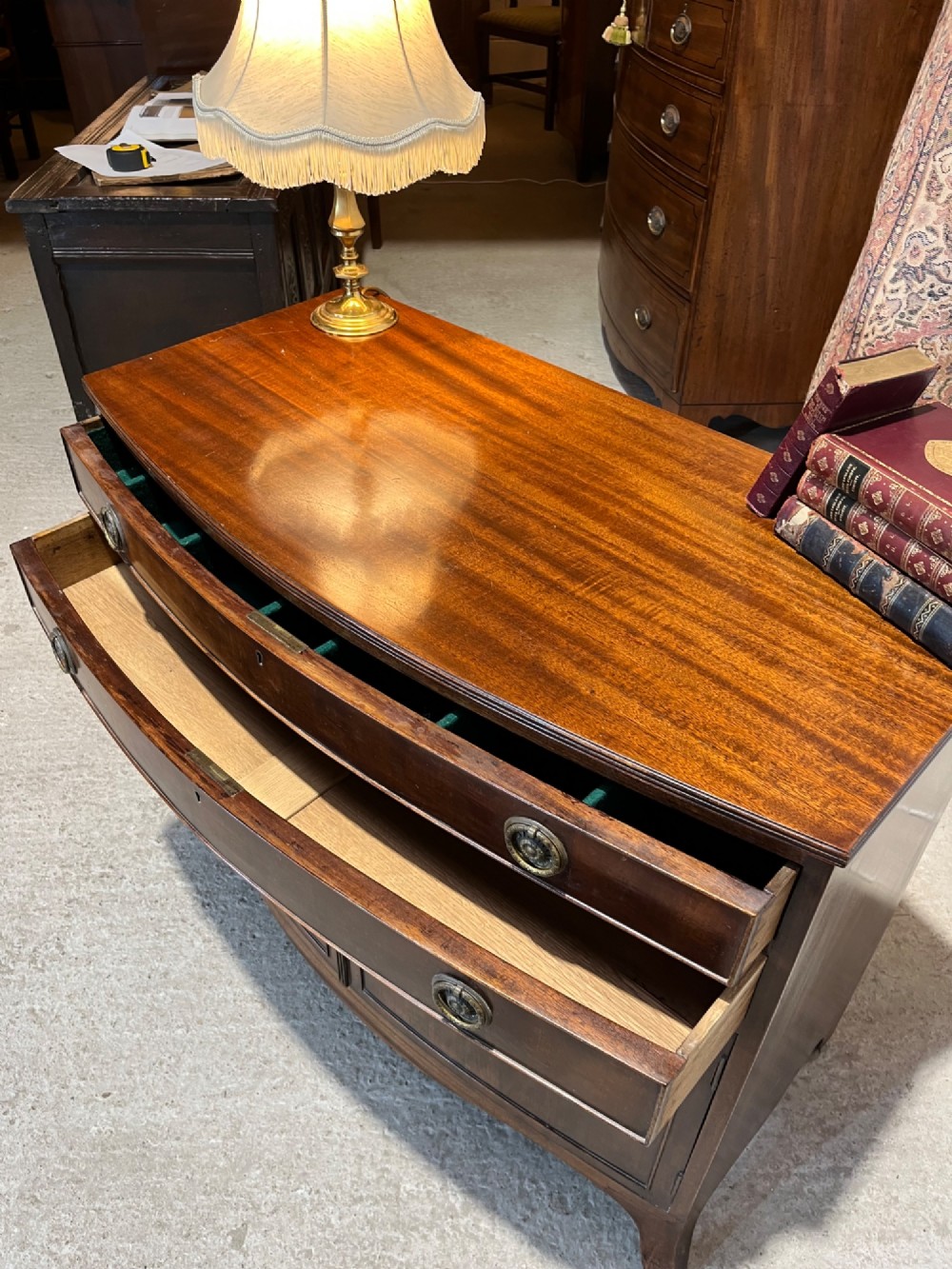 An early 20th-century mahogany bowfront cupboard with two top drawers featuring brass ring handles above a double-door lower compartment. View VII