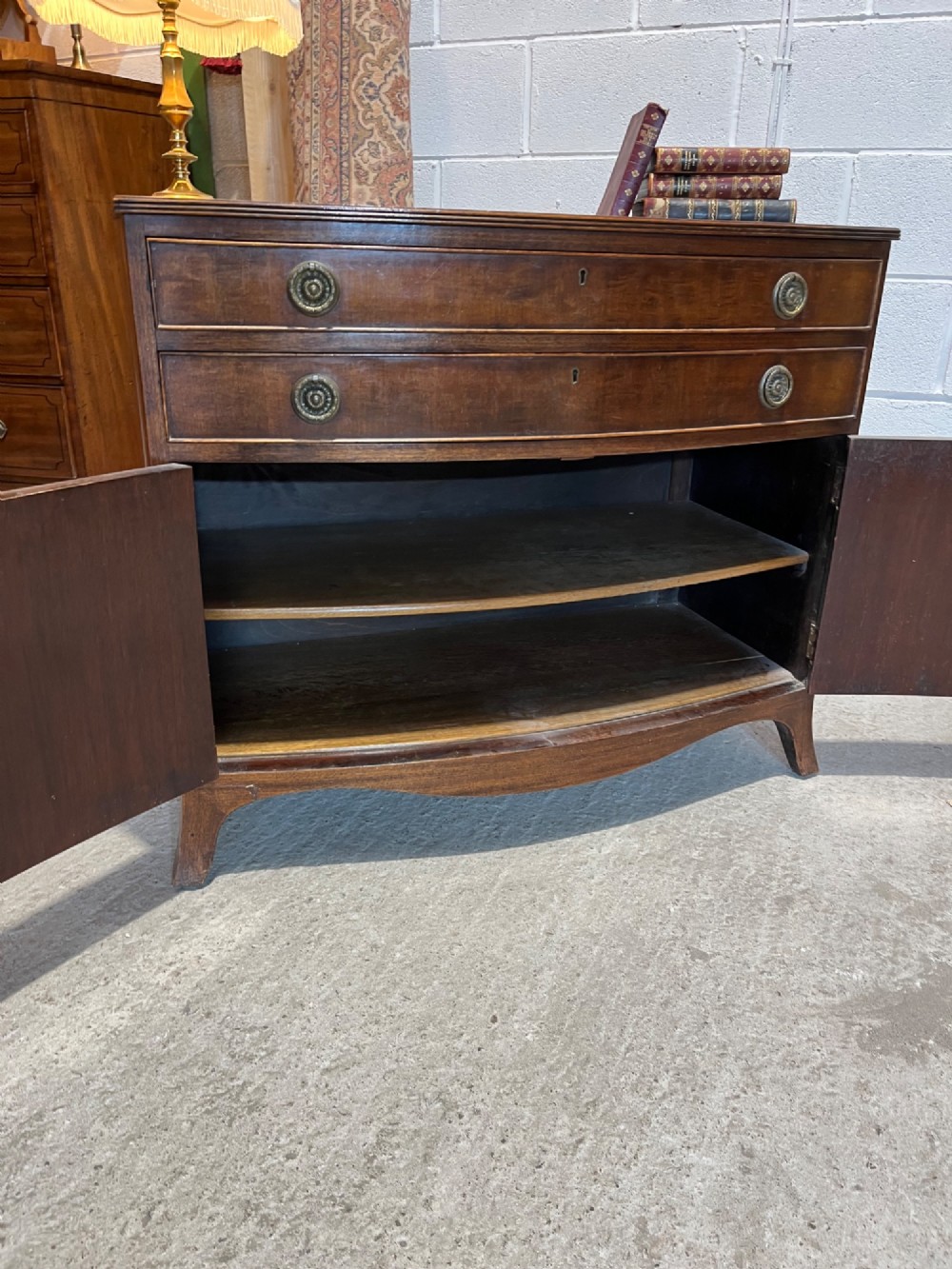 An early 20th-century mahogany bowfront cupboard with two top drawers featuring brass ring handles above a double-door lower compartment. View VIII