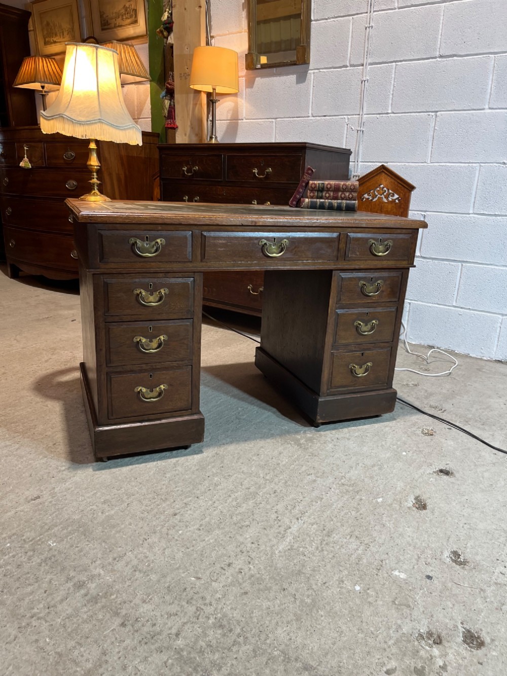 A late nineteenth-century dark oak pedestal desk featuring nine drawers with brass swan-neck handles and a green leather inset writing surface. View II