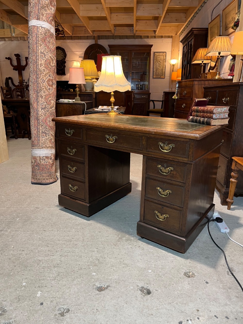A late nineteenth-century dark oak pedestal desk featuring nine drawers with brass swan-neck handles and a green leather inset writing surface. View V
