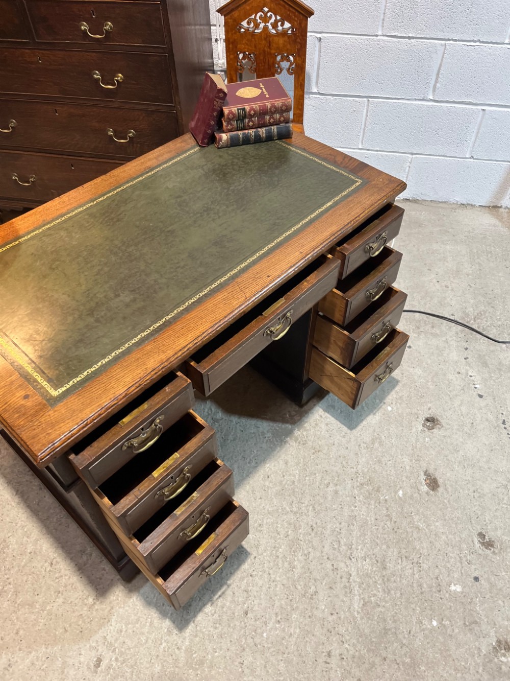 A late nineteenth-century dark oak pedestal desk featuring nine drawers with brass swan-neck handles and a green leather inset writing surface. View VIII