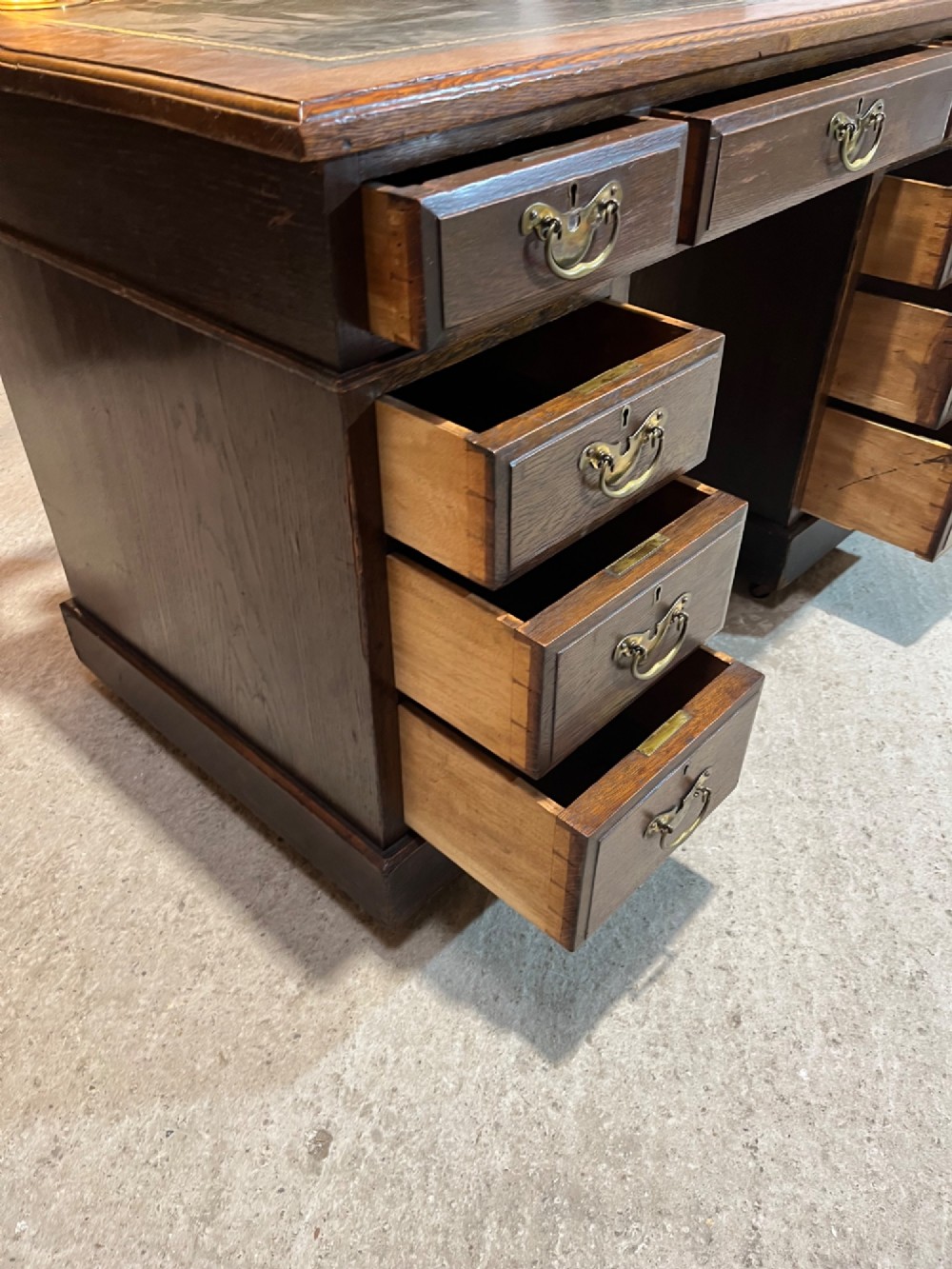A late nineteenth-century dark oak pedestal desk featuring nine drawers with brass swan-neck handles and a green leather inset writing surface. View IX