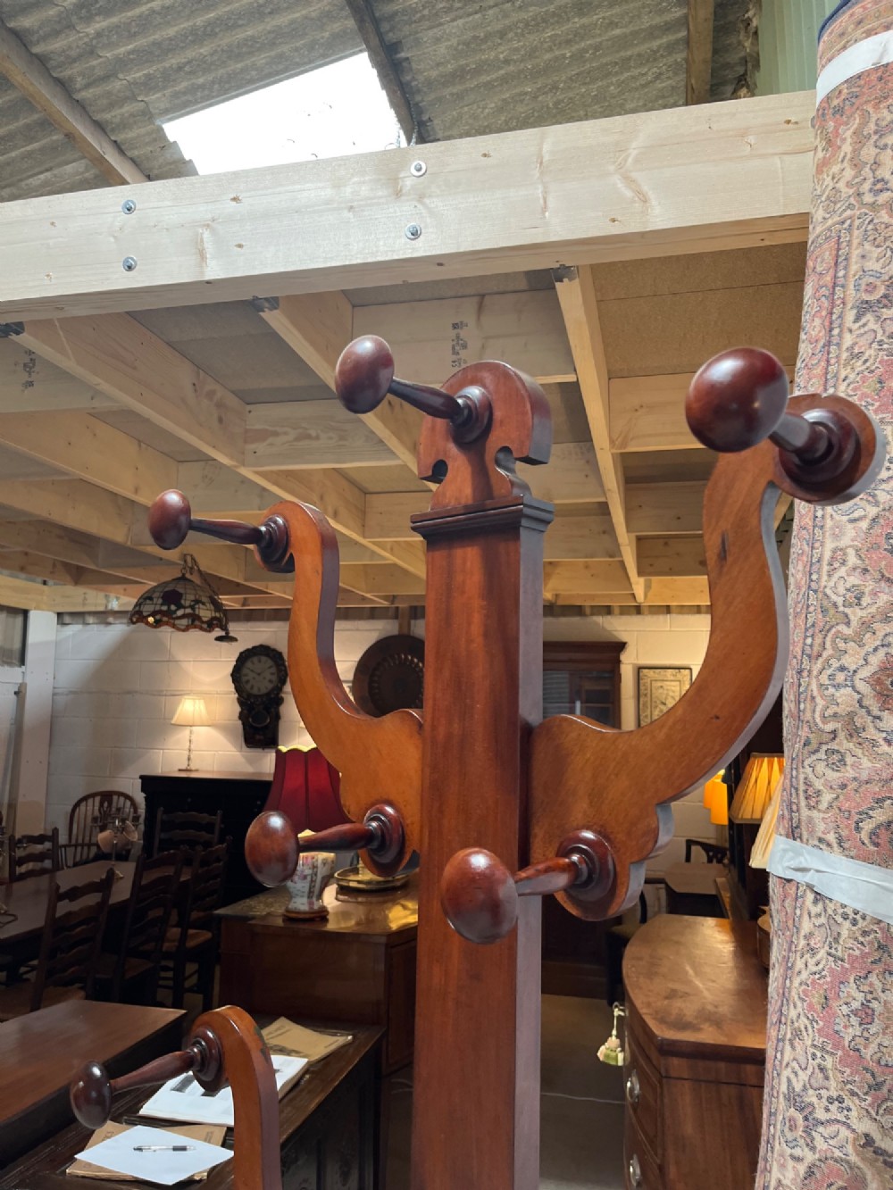 A 19th-century mahogany freestanding hall stand featuring turned wooden pegs on curved scroll arms above a lower umbrella holder with a drip tray. View V