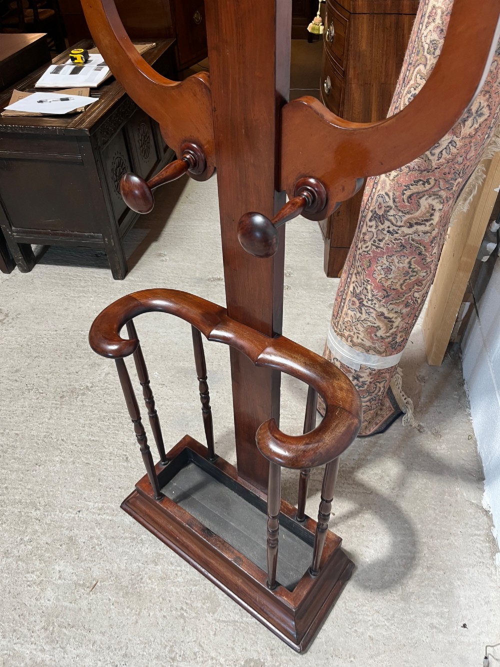 A 19th-century mahogany freestanding hall stand featuring turned wooden pegs on curved scroll arms above a lower umbrella holder with a drip tray. View VI