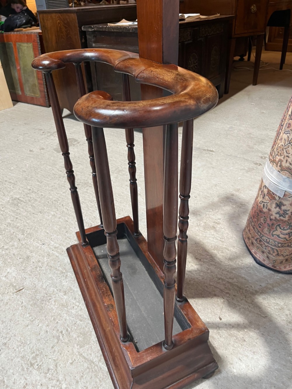 A 19th-century mahogany freestanding hall stand featuring turned wooden pegs on curved scroll arms above a lower umbrella holder with a drip tray. View VII