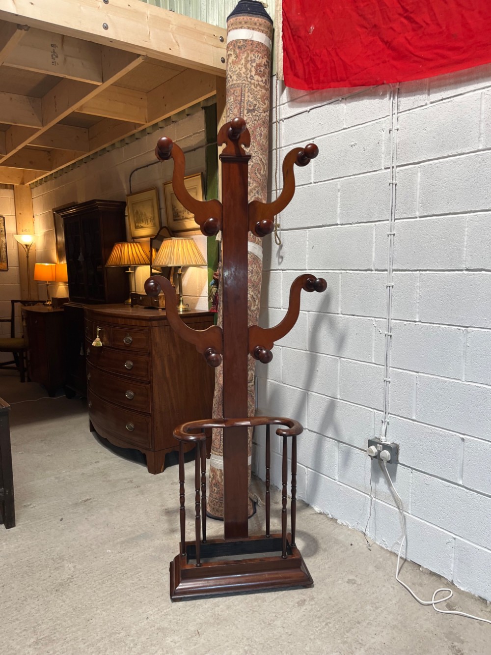 A 19th-century mahogany freestanding hall stand featuring turned wooden pegs on curved scroll arms above a lower umbrella holder with a drip tray. View IX