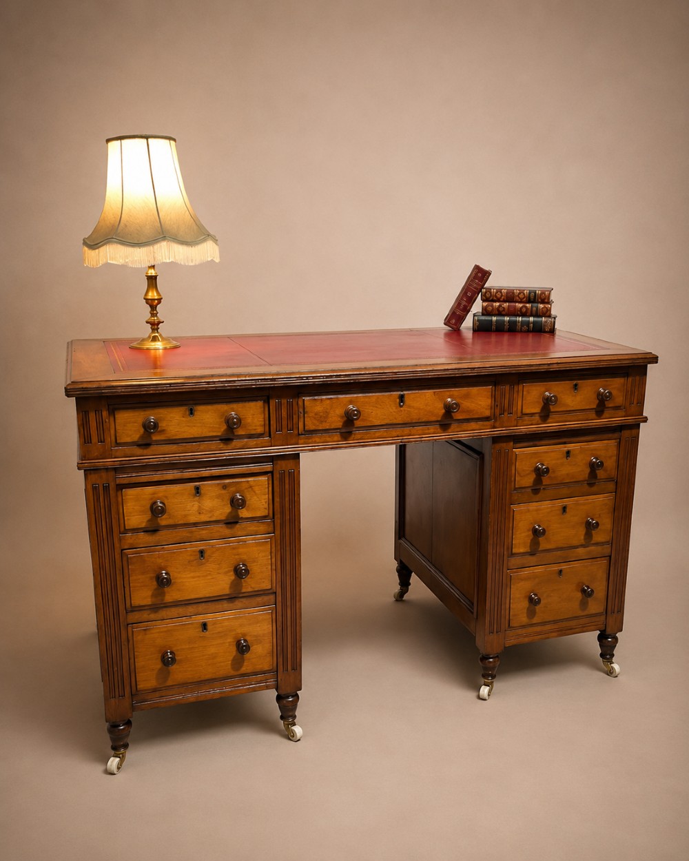 A 19th-century mahogany free-standing pedestal desk featuring a red leather top inset, multiple drawers with turned knobs, and brass castors.