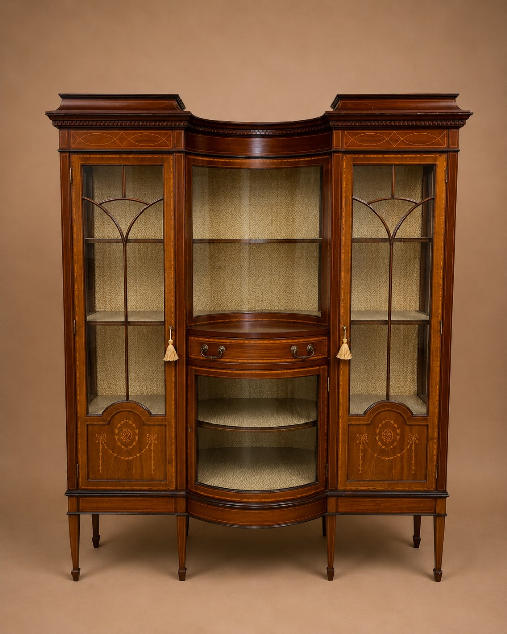 A late 19th-century inlaid mahogany display cabinet featuring glazed doors with astragal glazing, a concave centre section, satinwood marquetry swags, and slender square tapered legs.