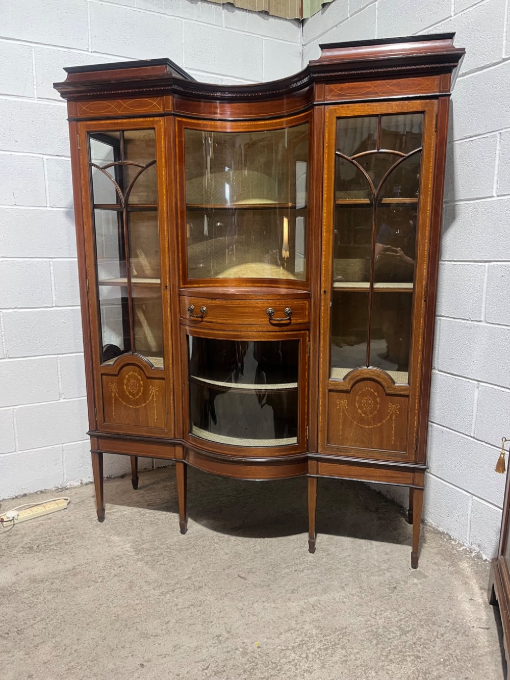 A late 19th-century inlaid mahogany display cabinet featuring glazed doors with astragal glazing, a concave centre section, satinwood marquetry swags, and slender square tapered legs. View III
