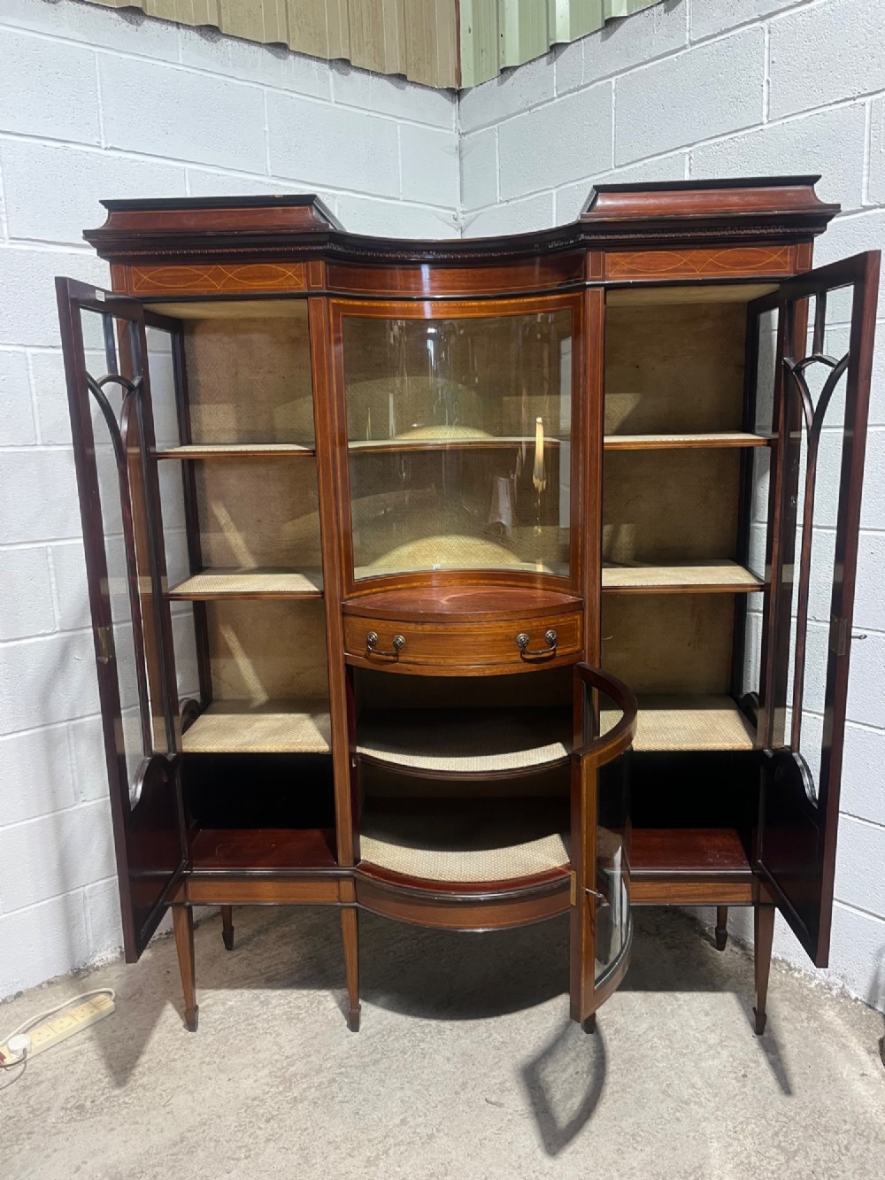 A late 19th-century inlaid mahogany display cabinet featuring glazed doors with astragal glazing, a concave centre section, satinwood marquetry swags, and slender square tapered legs. View XII