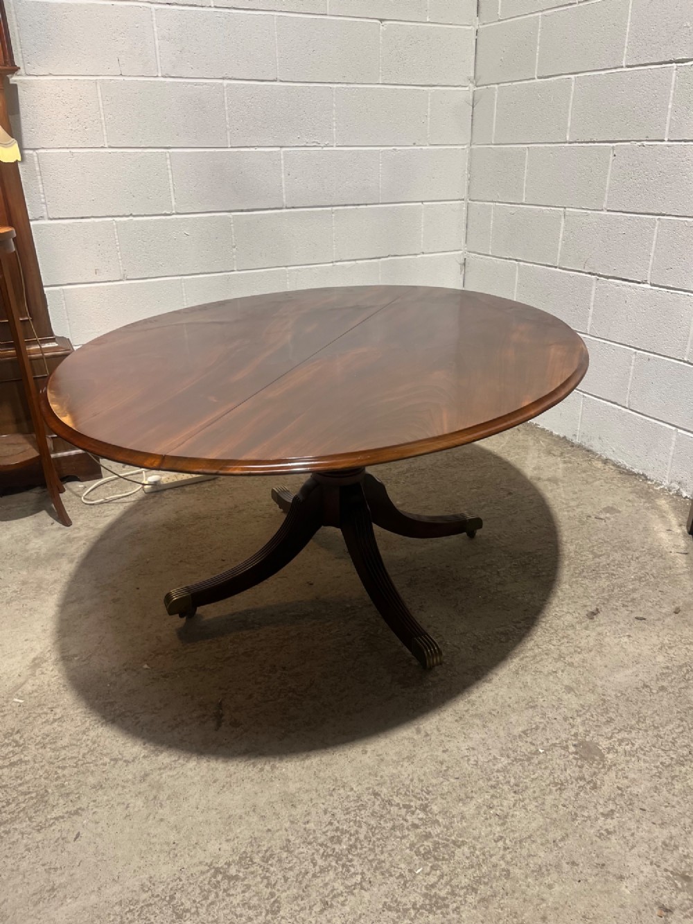 An oval Regency mahogany dining table featuring a central turned pedestal supported by four reeded sabre legs with brass casters. View X