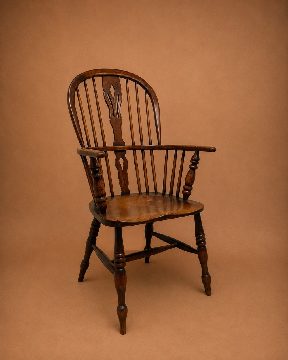 An antique 19th-century ash and elm high-back Windsor armchair featuring a hoop back with central pierced splat, turned arm supports, shaped saddle seat, and turned legs with an H-stretcher.
