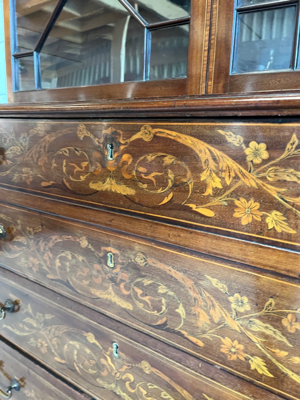 A 19th-century mahogany secretaire bookcase featuring an upper cabinet with geometric astragal glazed doors above a chest of drawers embellished with floral marquetry inlay. View V