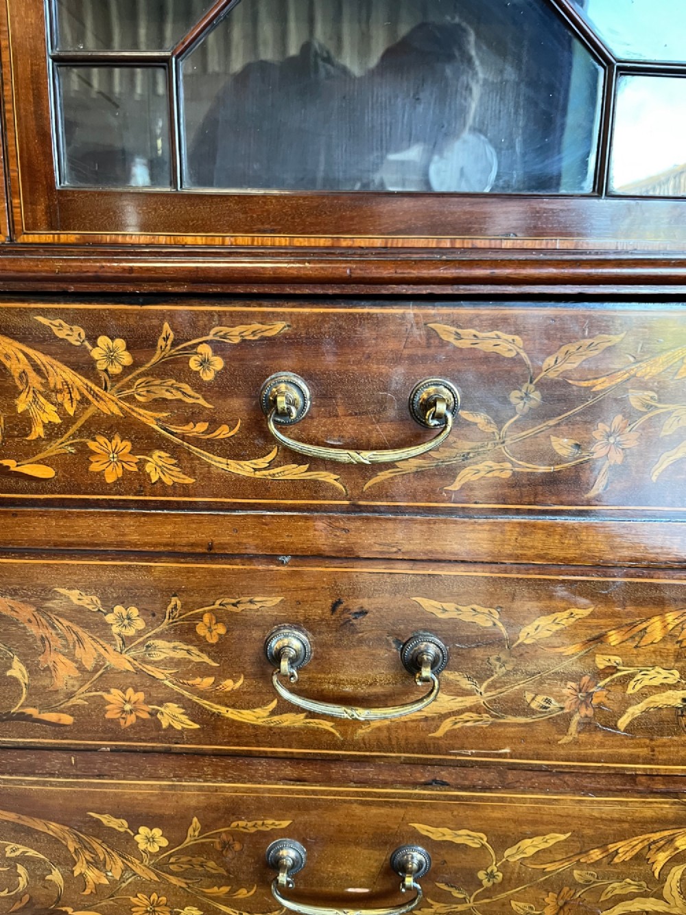 A 19th-century mahogany secretaire bookcase featuring an upper cabinet with geometric astragal glazed doors above a chest of drawers embellished with floral marquetry inlay. View VI