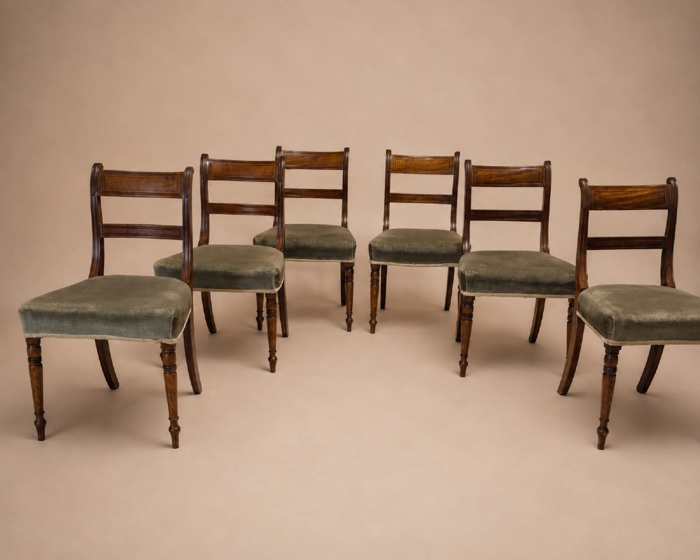 Set of six Regency mahogany dining chairs featuring horizontal bar backrests, green velvet seats, turned front legs, and splayed rear legs.