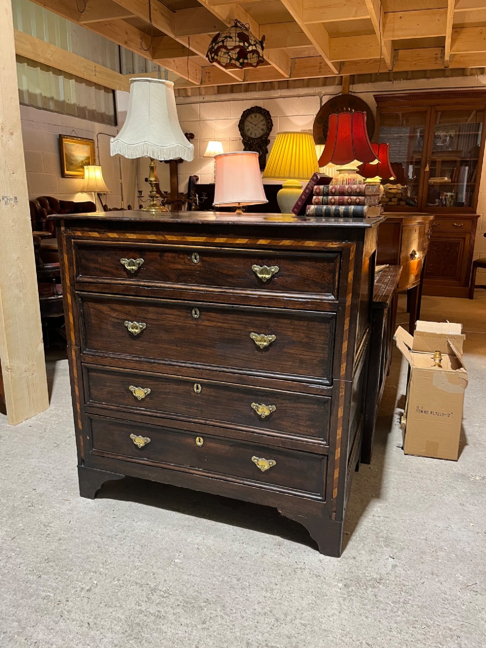 An early 18th-century dark oak chest of drawers featuring geometric inlay along the outer frame, four graduated drawers with brass handles, and bracket feet. View II