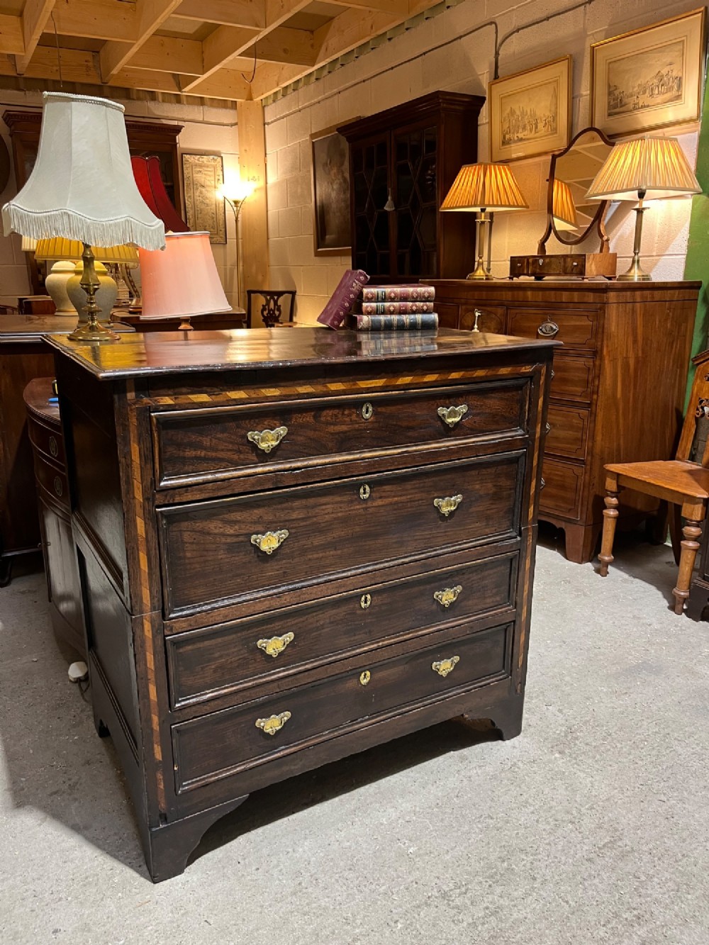An early 18th-century dark oak chest of drawers featuring geometric inlay along the outer frame, four graduated drawers with brass handles, and bracket feet. View V