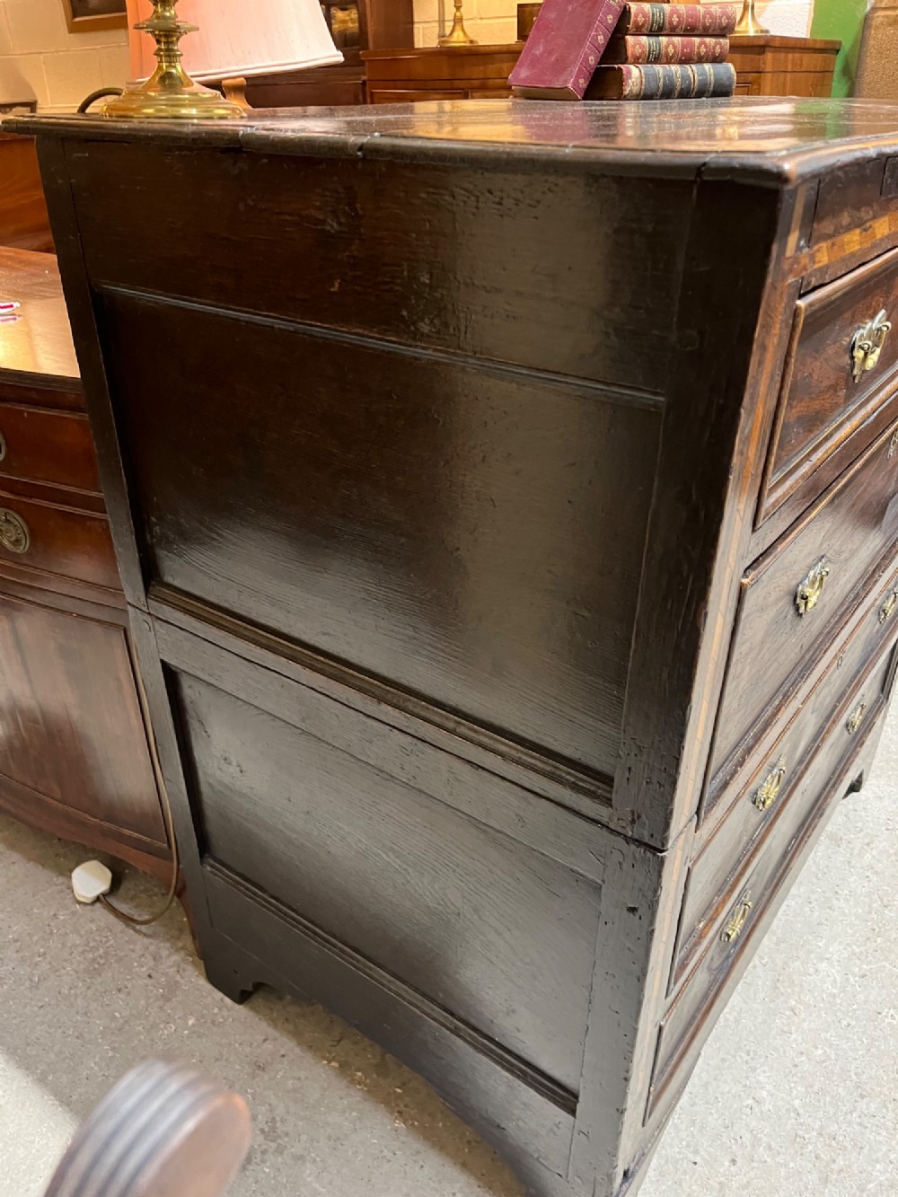 An early 18th-century dark oak chest of drawers featuring geometric inlay along the outer frame, four graduated drawers with brass handles, and bracket feet. View VII