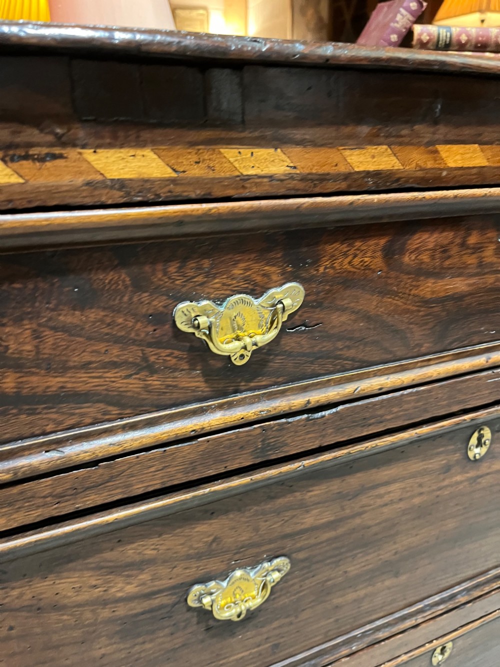 An early 18th-century dark oak chest of drawers featuring geometric inlay along the outer frame, four graduated drawers with brass handles, and bracket feet. View VIII