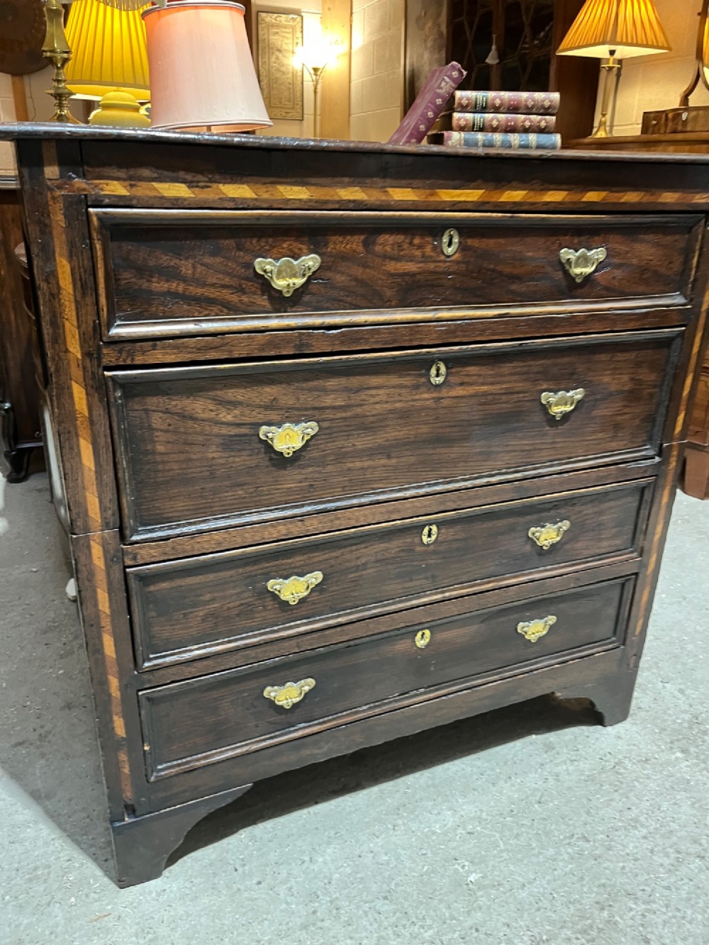 An early 18th-century dark oak chest of drawers featuring geometric inlay along the outer frame, four graduated drawers with brass handles, and bracket feet. View IX