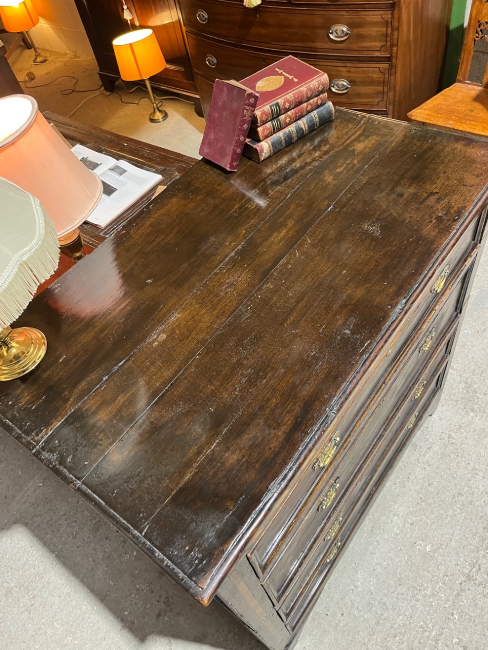 An early 18th-century dark oak chest of drawers featuring geometric inlay along the outer frame, four graduated drawers with brass handles, and bracket feet. View X