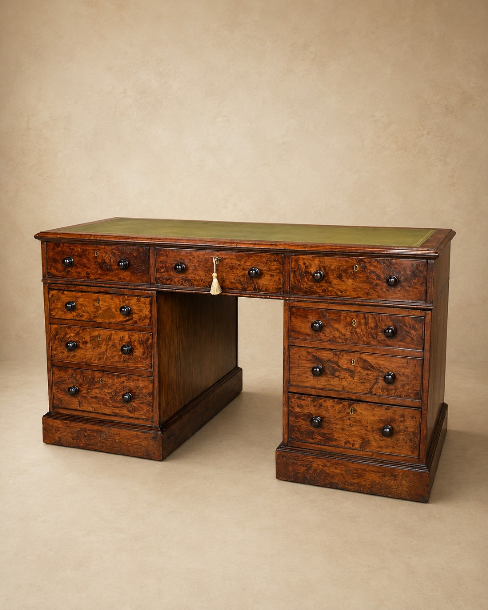 A nineteenth-century Victorian burr walnut pedestal desk featuring a green leather writing surface, multiple drawers with turned wooden handles, and a plinth base.
