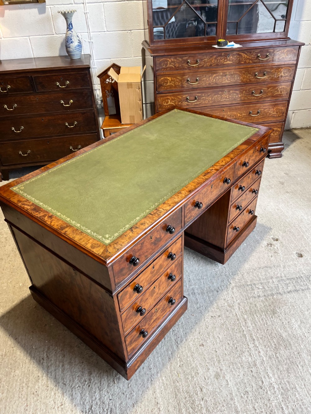 A nineteenth-century Victorian burr walnut pedestal desk featuring a green leather writing surface, multiple drawers with turned wooden handles, and a plinth base. View IV
