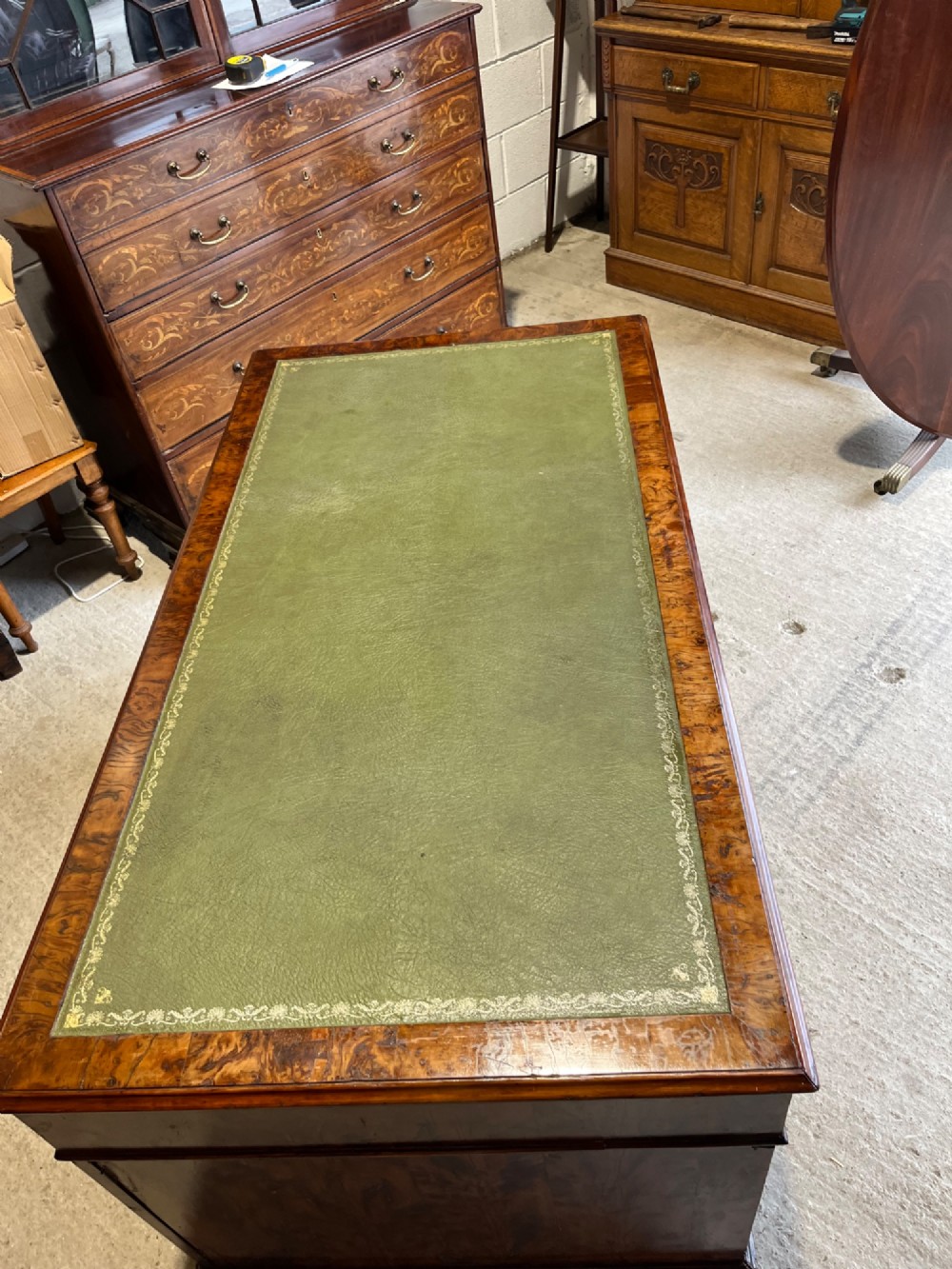 A nineteenth-century Victorian burr walnut pedestal desk featuring a green leather writing surface, multiple drawers with turned wooden handles, and a plinth base. View V